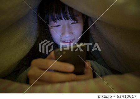 布団の中でスマホを見る子ども 63410017