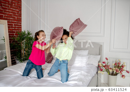 Two pretty girls fighting with pillows in the bedroom Two pretty girls fighting with pillows in the bedroom 63411524