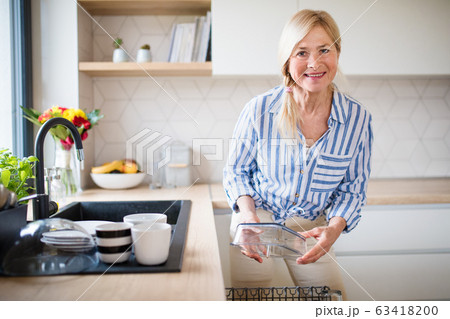 Portrait of senior woman washing dishes indoors at home. Portrait of senior woman washing dishes indoors at home. 63418200
