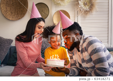 Father and mother help daughter blow out candles Father and mother help daughter blow out candles 63418271