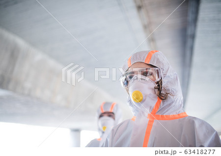 People with protective suits walking outdoors, coronavirus concept. People with protective suits walking outdoors, coronavirus concept. 63418277