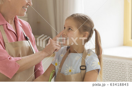 Mature woman touching her granddaughter's nose while cooking in kitchen 63418843
