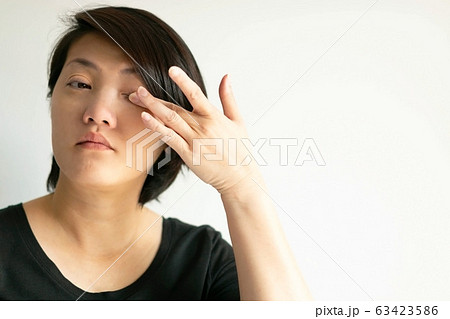An Asian woman uses a finger to wipe her eye on white background. 63423586