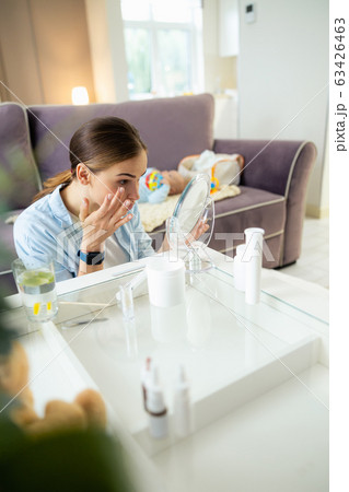Smiling young lady using face cream in room 63426463