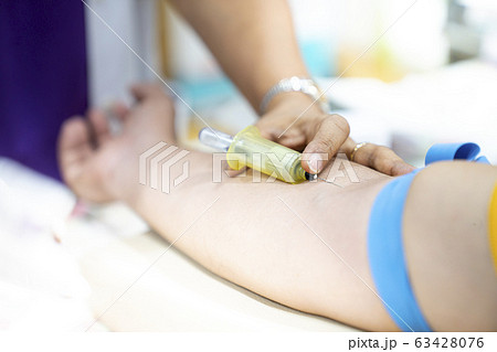 Medical person drawing blood with syringe and hypodermic needle from a patient. 63428076