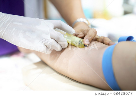 Medical person drawing blood with syringe and hypodermic needle from a patient. 63428077