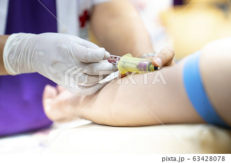 Medical person drawing blood with syringe and hypodermic needle from a patient. 63428078