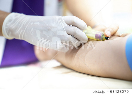 Medical person drawing blood with syringe and hypodermic needle from a patient. 63428079
