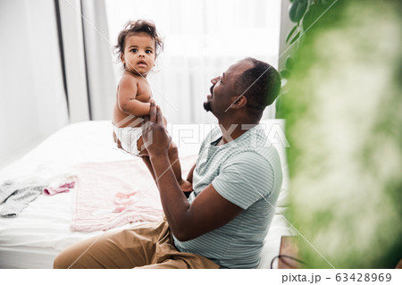 Happy Afro American man holding adorable baby girl in arms Happy Afro American man holding adorable baby girl in arms 63428969
