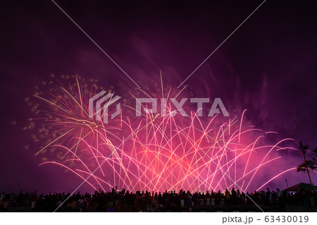 Crowd looks holiday fireworks in dark evening sky. 63430019
