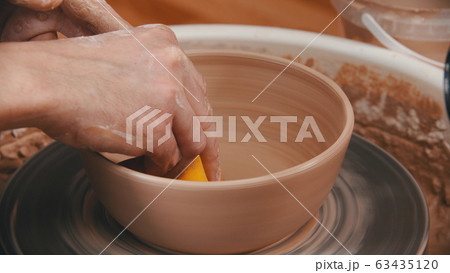 Pottery - the man is wiping the bottom of the bowl with a yellow sponge 63435120