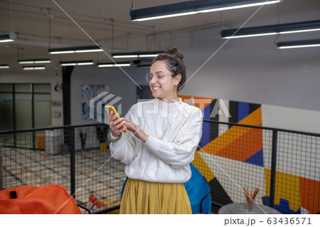 Young woman in eyeglasses, checking her phone, smiling 63436571
