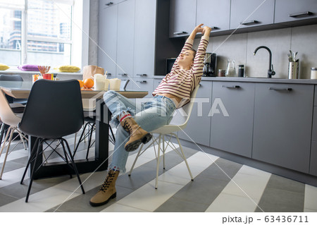 Young woman sitting at the kitchen table, stretching 63436711