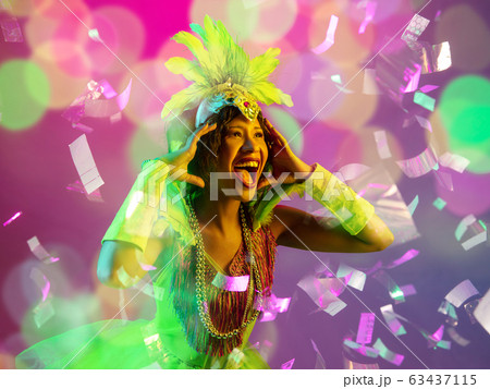 Beautiful young woman in carnival and masquerade costume in colorful neon lights on gradient background in flying confetti Beautiful young woman in carnival and masquerade costume in colorful neon lights on gradient background in flying confetti 63437115