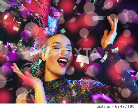 Beautiful young woman in carnival and masquerade costume in colorful neon lights on black background in flying confetti Beautiful young woman in carnival and masquerade costume in colorful neon lights on black background in flying confetti 63437190
