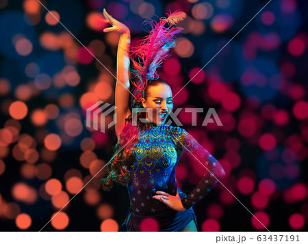 Beautiful young woman in carnival and masquerade costume in colorful neon lights on black background in flying confetti Beautiful young woman in carnival and masquerade costume in colorful neon lights on black background in flying confetti 63437191