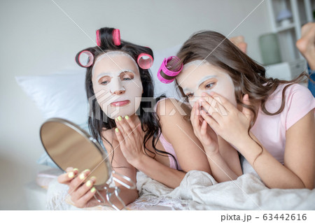 Mom and daughter with facial mask on their faces looking in the mirror 63442616