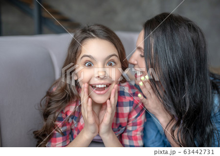 Dark-haired mom telling something interesting to her surprised daughter in the ear 63442731
