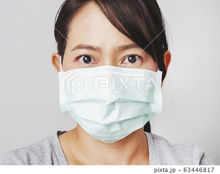 Asian woman was cold and sick, she wear green mask to prevent the virus covid. How to wear and pull mask from face. Covid 19 spread from Chinese people in Wuhan city. Close up face and eyes. 63446817