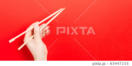 Wooden chopsticks in male hand on red background 63447153