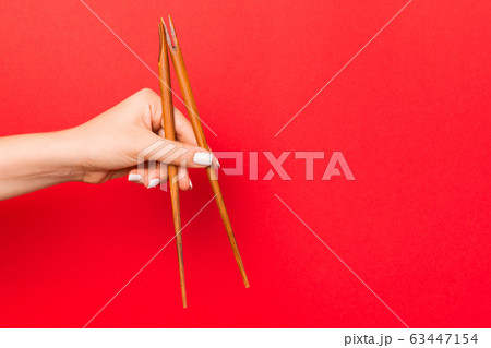 Wooden chopsticks holded with female hands on red 63447154
