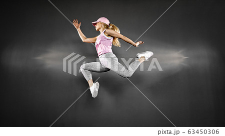 Young woman with fit body jumping and running against grey background. Female model in sportswear exercising 63450306