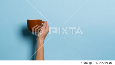 Woman holds in her hands a cup of coffee or tea drink blue bright background. Food drink concept. Copy space. 63454930