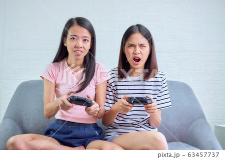 Two Asian woman sitting on sofa and playing games in the living room at home. 63457737