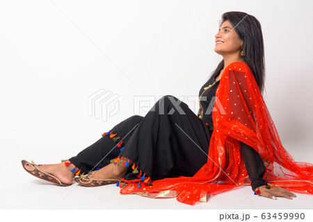Full body shot of happy young Persian woman thinking while sitting on the floor in traditional Full body shot of happy young Persian woman thinking while sitting on the floor in traditional 63459990