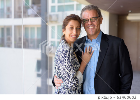 Happy Hispanic business couple smiling together by the window of office building 63460602