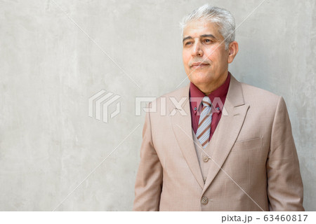 Mature Persian businessman with gray hair thinking against concrete wall outdoors 63460817