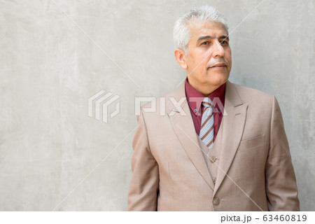 Mature Persian businessman with gray hair thinking against concrete wall outdoors 63460819