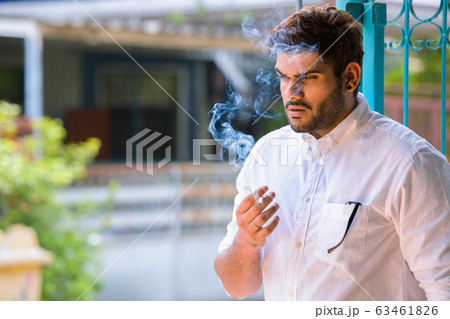 Young stressed bearded Indian man thinking while smoking outdoors Young stressed bearded Indian man thinking while smoking outdoors 63461826
