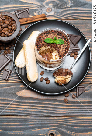 Classic tiramisu dessert in a glass cup, pieces of chocolate and savoiardi cookies on wooden background 63463850