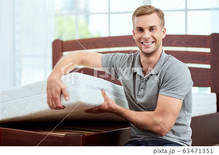 Healthy sleep. Young and happy handsome man showing big and comfortable ergonomic mattress at camera and smiling Healthy sleep. Young and happy handsome man showing big and comfortable ergonomic mattress at camera and smiling 63471351