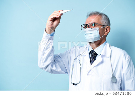 Senior doctor in glasses and a mask checks the temperature of the patient Senior doctor in glasses and a mask checks the temperature of the patient 63471580
