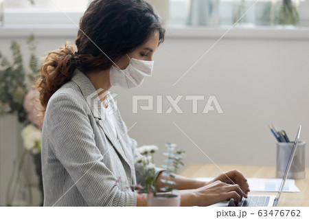Businesswoman in mask working on laptop at workplace Businesswoman in mask working on laptop at workplace 63476762