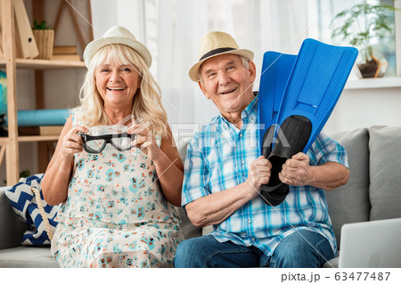 Senior couple sitting in travel agency sitting holding swimming mask and flippers smiling playful Senior couple sitting in travel agency sitting holding swimming mask and flippers smiling playful 63477487