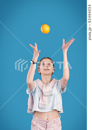 Energetic teenage girl throwing fresh orange while playing with it Energetic teenage girl throwing fresh orange while playing with it 63494054
