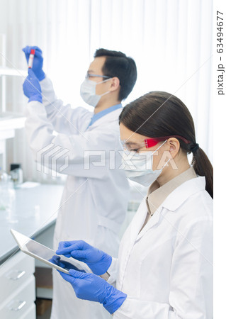 Female lab worker in protective mask, eyewear, gloves and whitecoat using tablet Female lab worker in protective mask, eyewear, gloves and whitecoat using tablet 63494677