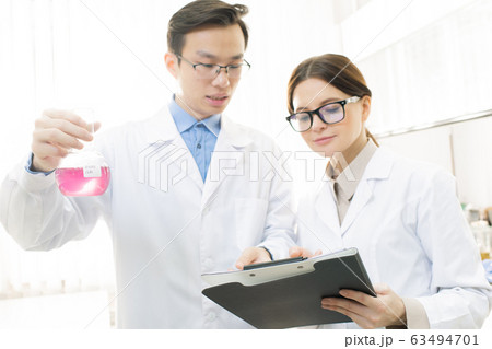 Young Asian male scientist or chemist holding beak with pink liquid substance Young Asian male scientist or chemist holding beak with pink liquid substance 63494701