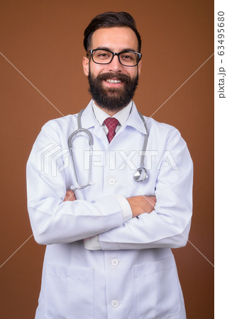 Young handsome bearded Persian man doctor against brown backgrou 63495680