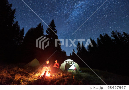 Couple enjoying starry night sky near campfire. 63497947
