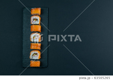 Granit board with sushi, filled with rolls of different kinds, next to stand sticks for sushi, red marinaginger and soy sauce. Granit board with sushi, filled with rolls of different kinds, next to stand sticks for sushi, red marinaginger and soy sauce. 63505265