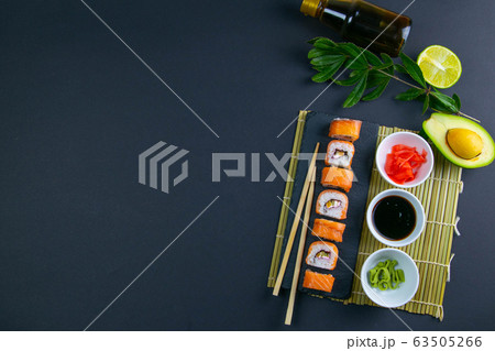 Granit board with sushi, filled with rolls of different kinds, next to stand sticks for sushi, red marinaginger and soy sauce. Granit board with sushi, filled with rolls of different kinds, next to stand sticks for sushi, red marinaginger and soy sauce. 63505266