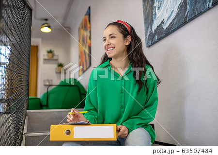 Young woman sitting on stairs with yellow folder on her lap. Young woman sitting on stairs with yellow folder on her lap. 63507484
