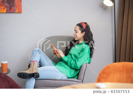 One woman looking into a tablet computer sitting in an armchair. One woman looking into a tablet computer sitting in an armchair. 63507553