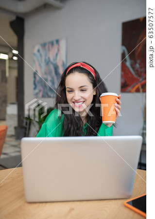 Joyful woman with coffee working at a laptop indoors. 63507577