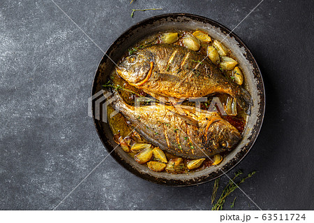 Baked sea bream or dorada with onion and herbs in pan on dark background Baked sea bream or dorada with onion and herbs in pan on dark background 63511724