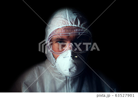 A doctor with a tired look in a respirator, glasses and a bacteriological protection suit. Low key. Concept of dedication to the medical profession A doctor with a tired look in a respirator, glasses and a bacteriological protection suit. Low key. Concept of dedication to the medical profession 63527901